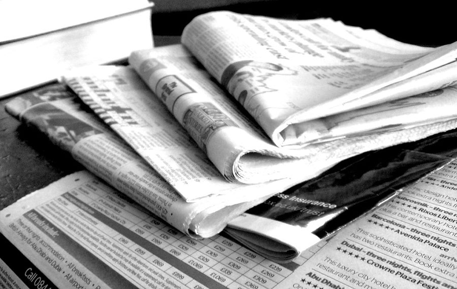 A black and white photo of a stack of newspapers fanned out on a dark table